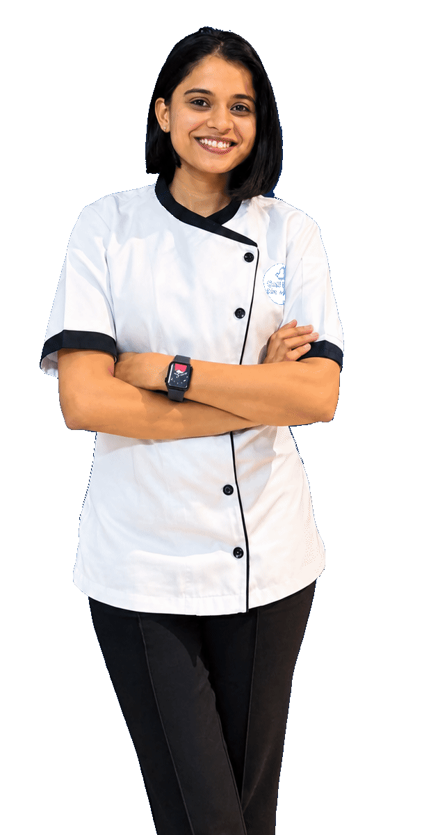 Bhavana Ballari, founder of Maison Bien Cake Studio, standing in white chef whites with her arms folded.