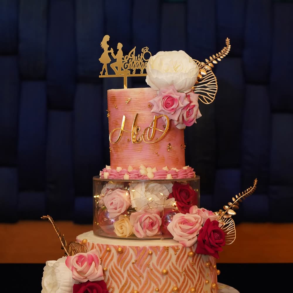 Three-tier engagement cake with blush textured buttercream, gold monogram initials, fresh roses and an illuminated transparent floral tier.