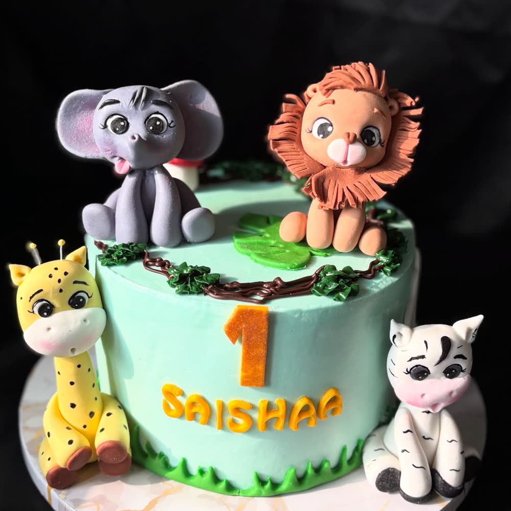 Mint-green first birthday cake topped with hand-modelled fondant jungle animals: an elephant, lion, giraffe and zebra, with piped foliage.