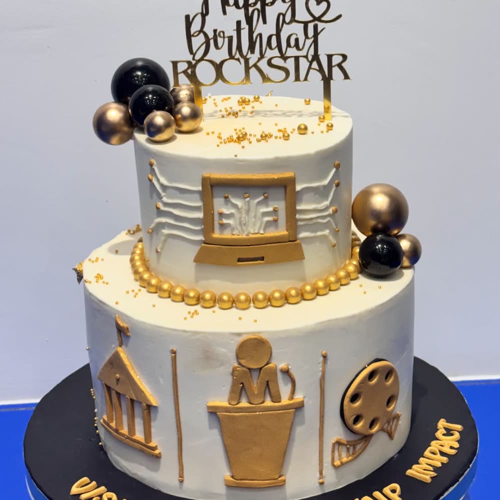 Two-tier ivory cake finished with gold and black spheres, gold pearl banding and hand-sculpted gold emblems representing a career milestone.